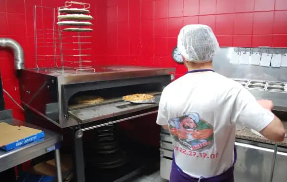 Le pizzaïolo enfourne une pizza dans le four de Pizza Délice